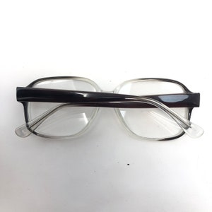 K&ouml;nnte beinhalten: Eine Brille mit transparentem Rahmen und dunkelbraunen B&uuml;geln. Die Brille hat eine rechteckige Form. Die Aufnahme zeigt die Brille von oben, wobei die Gl&auml;ser und das Design des Rahmens hervorgehoben werden.