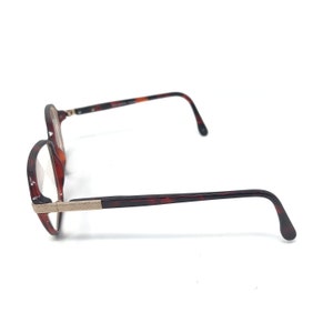 May include: Brown tortoiseshell eyeglasses with a round frame and rectangular lenses. The temples and frame arms are a dark brown tortoiseshell pattern. The bridge and hinges are a silver color.