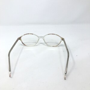 May include: Clear oval eyeglasses with silver-toned arms. The frames have a subtle pattern of red, white, and blue dots along the top and bottom rims. The glasses are set against a plain white background.