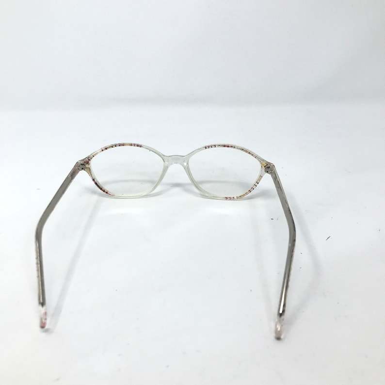 May include: Clear oval eyeglasses with silver-toned arms. The frames have a subtle pattern of red, white, and blue dots along the top and bottom rims. The glasses are set against a plain white background.