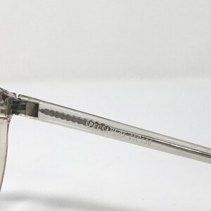 Puede incluir: Primer plano de una montura de gafas transparente con el texto "SPECSAVERS SSC756" impreso en la varilla. La montura es de material transparente y tiene forma rectangular.