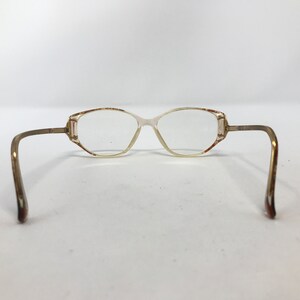 May include: Vintage eyeglasses with a light brown frame and clear lenses. The glasses have a rectangular shape with rounded edges and thin, curved temples. The frame has a subtle, two-tone color scheme.