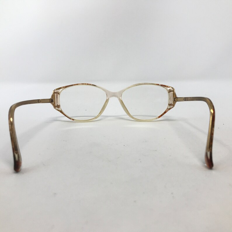 May include: Vintage eyeglasses with a light brown frame and clear lenses. The glasses have a rectangular shape with rounded edges and thin, curved temples. The frame has a subtle, two-tone color scheme.