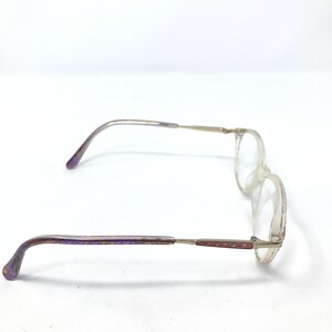 May include: Clear-framed eyeglasses with a rectangular lens shape. The temples are silver with purple and red accents. The earpieces are purple. The glasses are set against a white background.