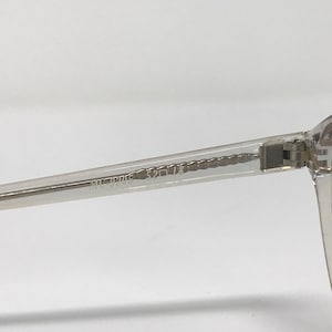 Puede incluir: Primer plano de una montura de gafas transparente. La patilla de las gafas tiene los n&uacute;meros "52 18" impresos. La montura est&aacute; hecha de un material transparente.