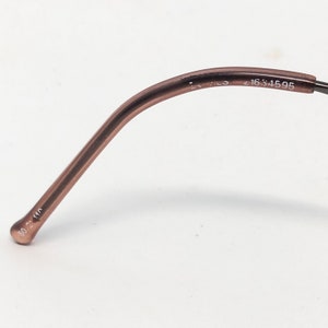 Puede incluir: Primer plano de un par de gafas. La montura es de color marr&oacute;n apagado. La patilla tiene los n&uacute;meros "1634595" impresos. El extremo de la patilla tiene los n&uacute;meros "50 2 140" impresos.