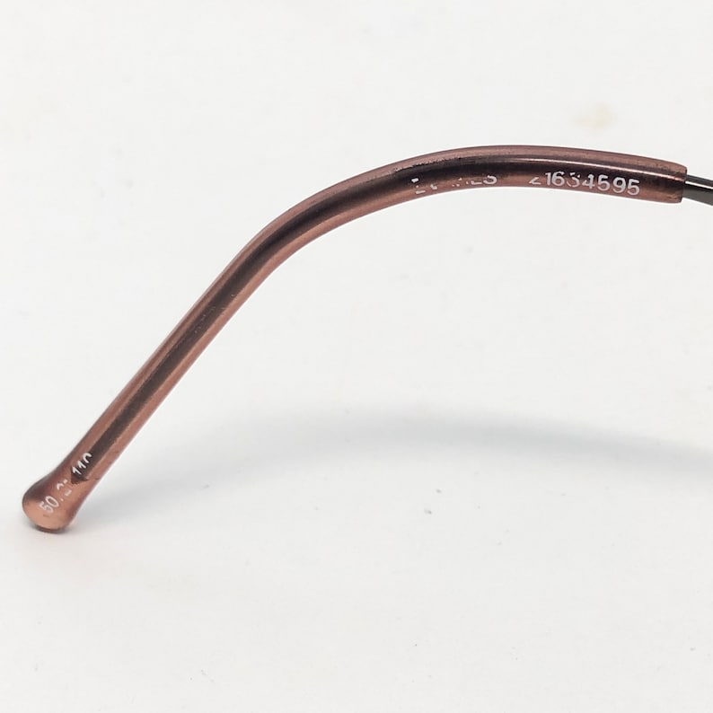 Puede incluir: Primer plano de un par de gafas. La montura es de color marr&oacute;n apagado. La patilla tiene los n&uacute;meros "1634595" impresos. El extremo de la patilla tiene los n&uacute;meros "50 2 140" impresos.