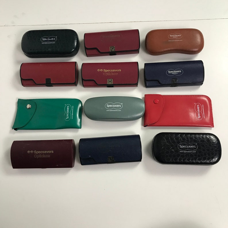 May include: A collection of various colored eyeglass cases, including green, red, blue, and black. Each case has the "Specsavers" logo printed on it. The cases are in different shapes and sizes, with some having a button closure.
