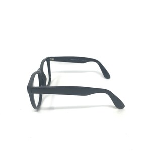 May include: Black eyeglasses with a rectangular frame and curved temples. The glasses are made of a matte black material and are set against a white background. The side of the frame has text printed on it.