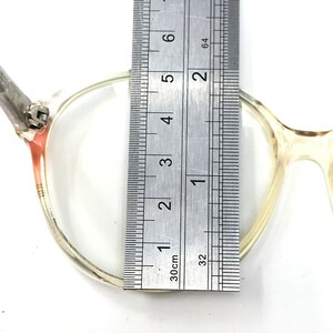 Puede incluir: Primer plano de unas gafas redondas transparentes con una regla que mide el ancho del marco a 4,5 cm.