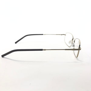 May include: A pair of eyeglasses with a silver metal frame and black temples. The lenses are clear, and the glasses are designed for vision correction. The side view shows the sleek, modern design of the eyewear.