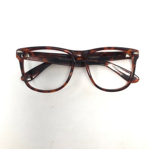 May include: Tortoiseshell-patterned eyeglasses with a rectangular frame. The glasses have a dark brown and amber color scheme. The brand name "SPECSAVER" is visible on the frame. The glasses are set against a white background.