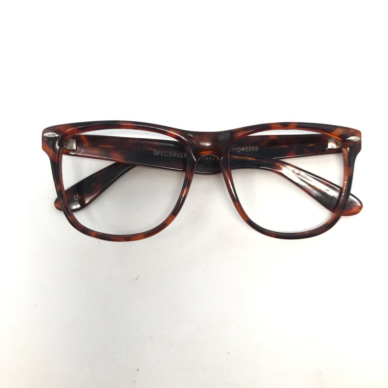May include: Tortoiseshell-patterned eyeglasses with a rectangular frame. The glasses have a dark brown and amber color scheme. The brand name "SPECSAVER" is visible on the frame. The glasses are set against a white background.