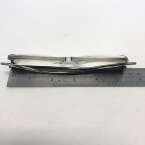 K&ouml;nnte beinhalten: Brille mit transparentem Rahmen und schwarzem B&uuml;gel liegt auf einem Lineal. Das Lineal zeigt Messungen in Zentimetern an. Die Brille ist etwa 14 cm breit.