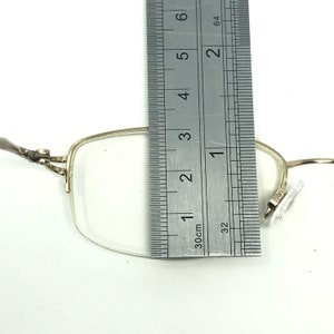 May include: Silver-toned metal glasses with clear lenses. The glasses are measured with a ruler, showing a width of approximately 1 3/8 inches.