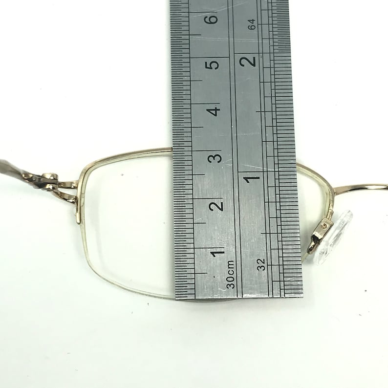 May include: Silver-toned metal glasses with clear lenses. The glasses are measured with a ruler, showing a width of approximately 1 3/8 inches.