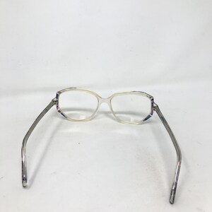 Puede incluir: Gafas transparentes con montura de color claro y lentes rectangulares. Las patillas son plateadas con un patr&oacute;n sutil. La montura tiene un patr&oacute;n decorativo en tonos azules, morados y blancos cerca de las bisagras.
