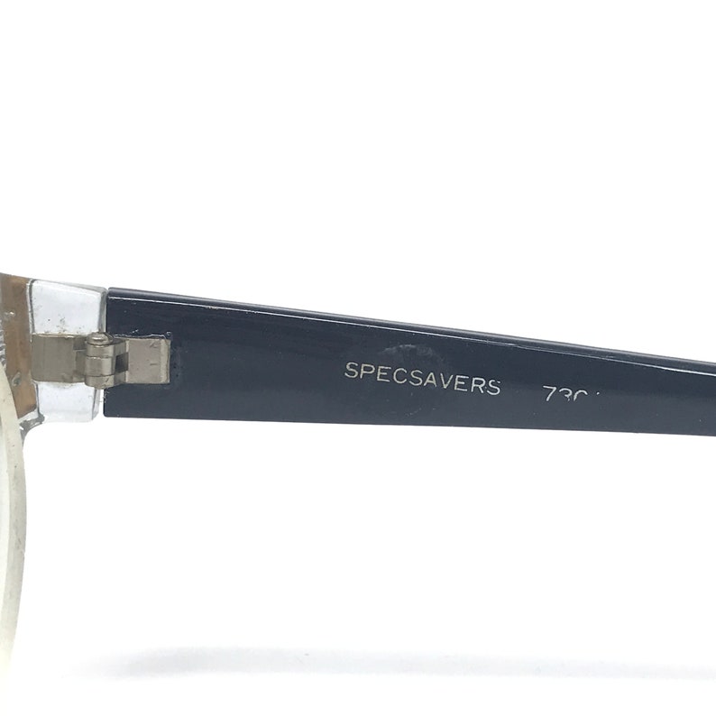 May include: Close-up of the arm of a pair of eyeglasses with a black frame and the text "SPECSAVERS 730C" printed on the arm.