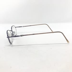 May include: A pair of eyeglasses with a thin, oval-shaped frame. The frame is a dark, muted color, with slender, light brown temples. The lenses are clear, and the glasses are set against a white background.