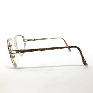 May include: A pair of gold-toned eyeglasses with clear plastic frames and a patterned design on the arms.