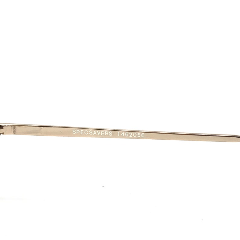 May include: Close-up of a gold-colored eyeglass frame arm. The text "SPECSAVERS 1462056" is printed in black on the arm. The frame appears to be made of metal and has a sleek, modern design.