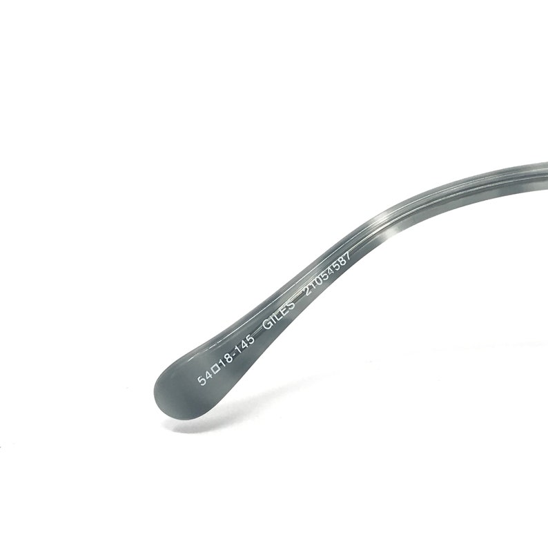Puede incluir: Primer plano de la patilla de unas gafas. La patilla es de color gris claro con un patr&oacute;n veteado. El texto "54▢18-145 GILES 21054587" est&aacute; impreso en blanco en la patilla.