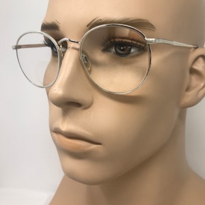 Peut inclure: Lunettes &agrave; monture argent&eacute;e avec verres ronds. Les lunettes ont une monture m&eacute;tallique fine et sont pr&eacute;sent&eacute;es sur un mannequin. Les verres sont clairs et le design g&eacute;n&eacute;ral est minimaliste et classique. Les lunettes sont un accessoire &eacute;l&eacute;gant.