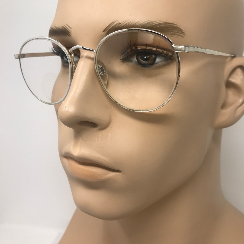 Peut inclure: Lunettes &agrave; monture argent&eacute;e avec verres ronds. Les lunettes ont une monture m&eacute;tallique fine et sont pr&eacute;sent&eacute;es sur un mannequin. Les verres sont clairs et le design g&eacute;n&eacute;ral est minimaliste et classique. Les lunettes sont un accessoire &eacute;l&eacute;gant.