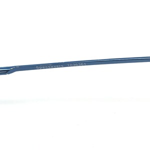 May include: Close-up of a section of blue eyeglasses frame. The text "Specsavers" and the number "1036361" are printed on the frame. The frame is a thin, sleek design, likely made of metal, with a modern aesthetic.