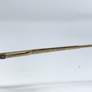 May include: Close-up of a gold-colored eyeglass frame arm. The text "SPECSAVERS TC 1333153" is printed on the arm. The frame is set against a white background.