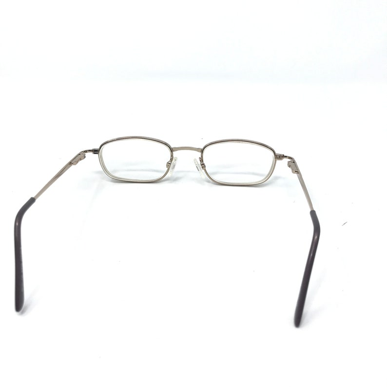 May include: Silver-framed eyeglasses with rectangular lenses. The glasses have a thin metal frame and dark gray temple arms. The lenses are clear, and the glasses are set against a white background.