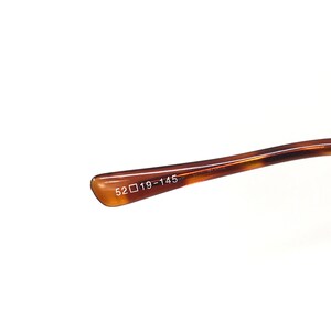 May include: Close-up of the brown tortoise shell temple arm of a pair of eyeglasses. The temple arm is marked with the text "52□19-145".
