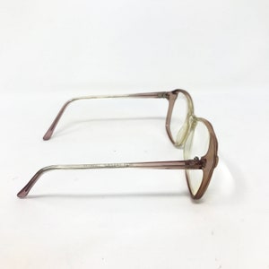 May include: A pair of vintage eyeglasses with a light brown frame and clear lenses. The arms of the glasses are a gradient, transitioning from light brown to clear. The glasses are set against a white background.