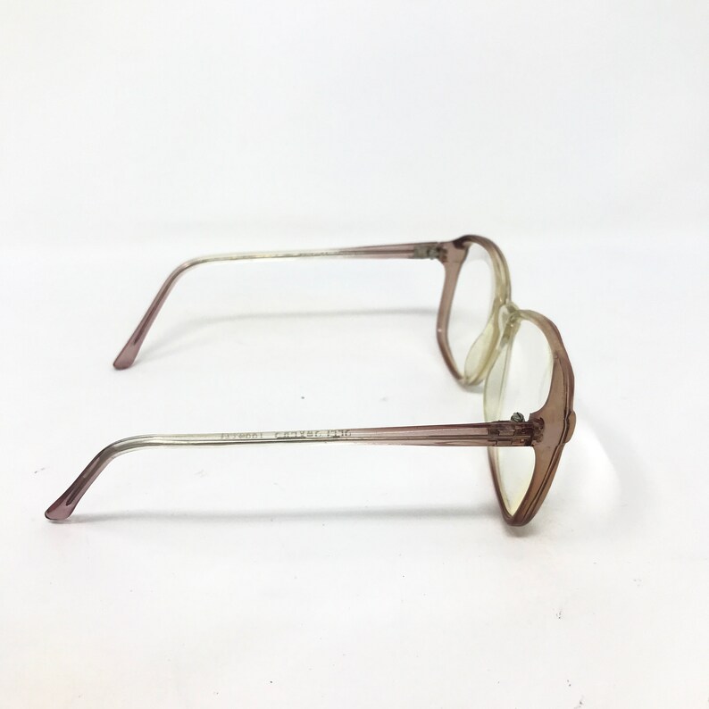 May include: A pair of vintage eyeglasses with a light brown frame and clear lenses. The arms of the glasses are a gradient, transitioning from light brown to clear. The glasses are set against a white background.