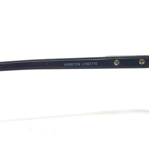 May include: Close-up of a black eyeglass frame arm with the text "WINSTON 21001710" printed in white. The frame has small silver screws and a silver accent.
