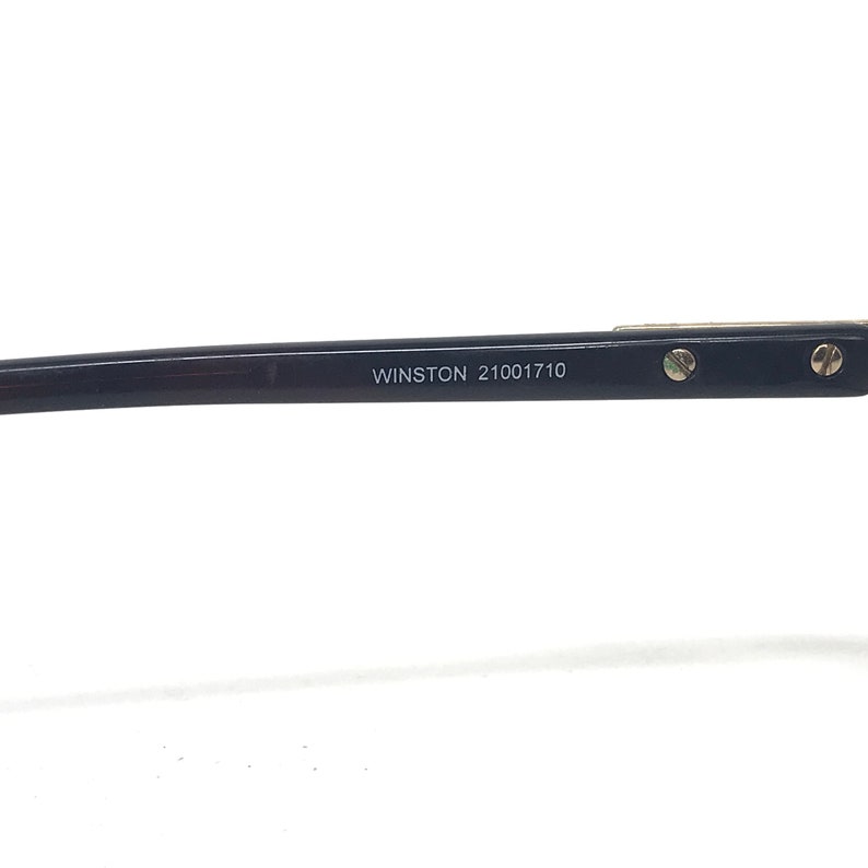 May include: Close-up of a black eyeglass frame arm with the text "WINSTON 21001710" printed in white. The frame has small silver screws and a silver accent.