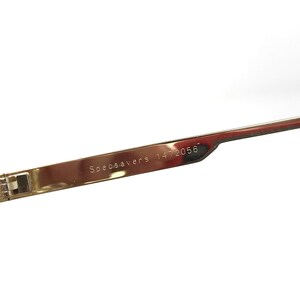 May include: Close-up of the arm of a pair of gold-tone glasses with the text "Specsavers 1472056" engraved on the metal.
