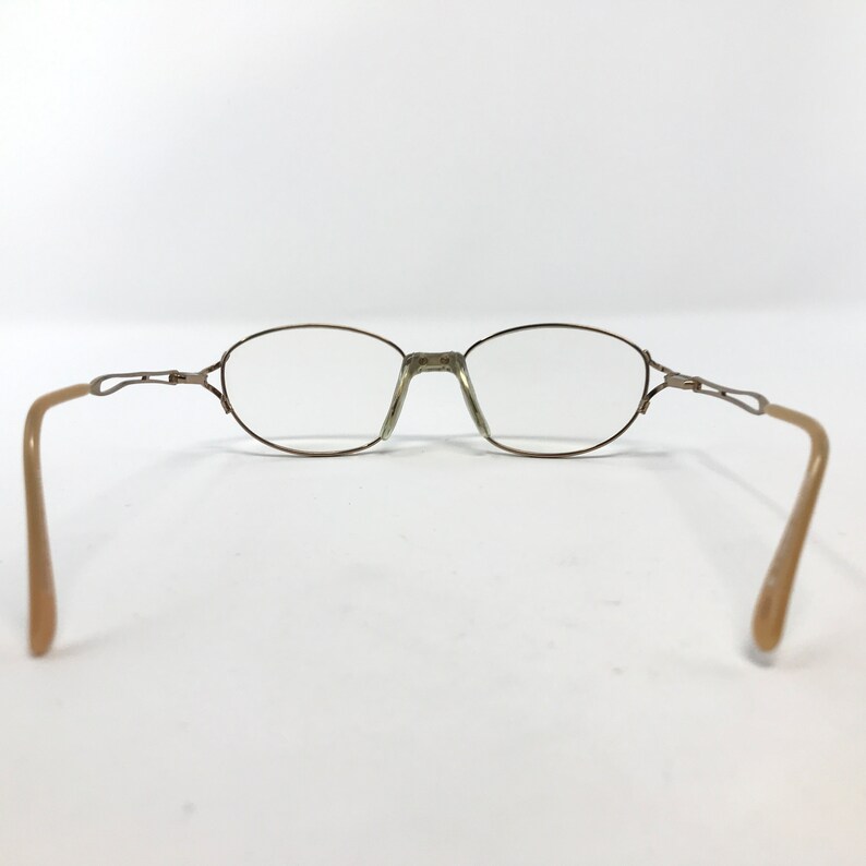 Peut inclure: Une paire de lunettes de vue ovales avec une monture en m&eacute;tal dor&eacute; et des branches en plastique beige.