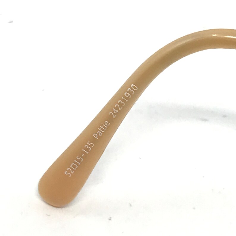 Peut inclure: Gros plan de l'int&eacute;rieur d'une monture de lunettes de couleur beige avec le texte "52015-135 Pattie 24231930" imprim&eacute; dessus.