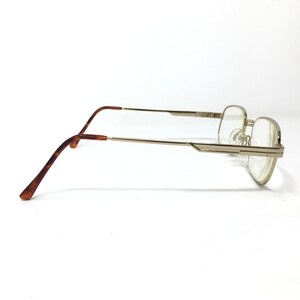 May include: Gold-tone metal eyeglasses with brown tortoise shell temple tips. The glasses have a rectangular frame and clear lenses.