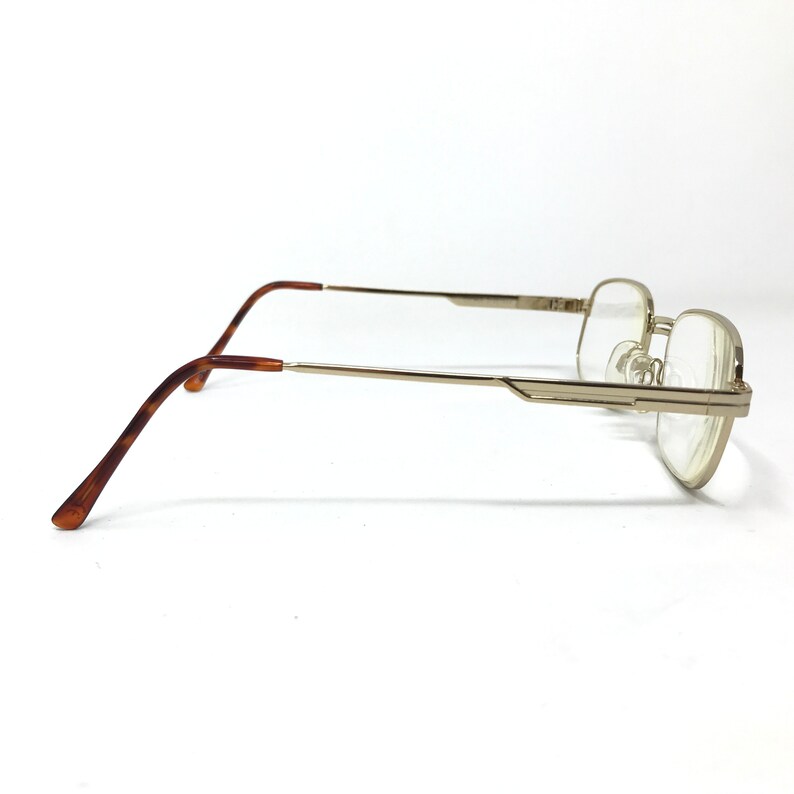 May include: Gold-tone metal eyeglasses with brown tortoise shell temple tips. The glasses have a rectangular frame and clear lenses.