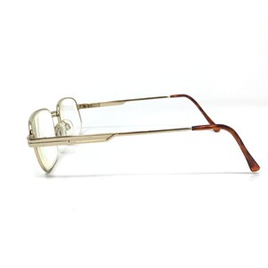 May include: Gold-tone metal eyeglasses with brown plastic temple tips. The glasses have a rectangular frame and clear lenses.