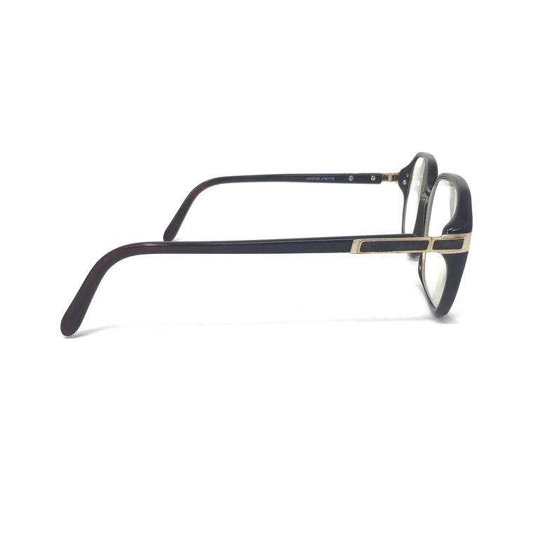 May include: Eyeglasses with a dark brown frame and temples. The lenses are clear, and the frame has a rectangular shape with gold-coloured accents. The glasses are viewed from the side against a white background.