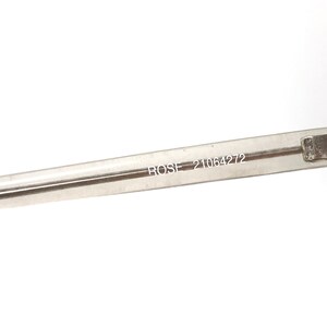 May include: Close-up of a clear, rectangular eyeglass frame arm. The text "ROSE 21064272" is printed in a small, black font on the arm. The frame is set against a bright white background.