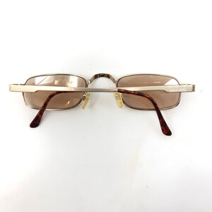 May include: Rectangular sunglasses with a silver metal frame and brown tinted lenses. The temples have a tortoiseshell pattern. The glasses are viewed from the back, showing the bridge and nose pads.