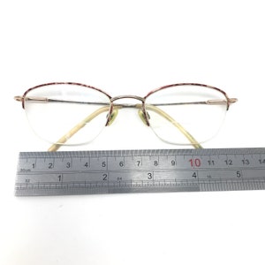 May include: Gold-tone half-rim eyeglasses with clear lenses. The top rims have a red and white speckled pattern. A metal ruler shows the glasses are approximately 5 inches wide.