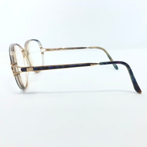 May include: Vintage eyeglasses with a gold-tone frame and clear lenses. The temples feature a dark blue and green marbled design. The glasses have a square shape and are set against a white background.