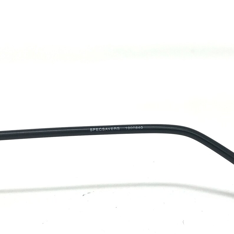 Puede incluir: Primer plano de una patilla de gafas negra. El texto "SPECSAVERS 1000840" est&aacute; impreso en blanco en la patilla. La montura est&aacute; sobre un fondo blanco.
