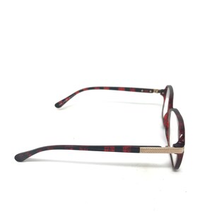 May include: Round-framed eyeglasses with a tortoiseshell pattern in shades of red and black. The temples have a black and red striped design. The frame features a gold-colored metal accent near the hinges. The glasses are set against a white background.