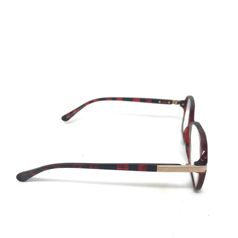 May include: Round-framed eyeglasses with a tortoiseshell pattern in shades of red and black. The temples have a black and red striped design. The frame features a gold-colored metal accent near the hinges. The glasses are set against a white background.